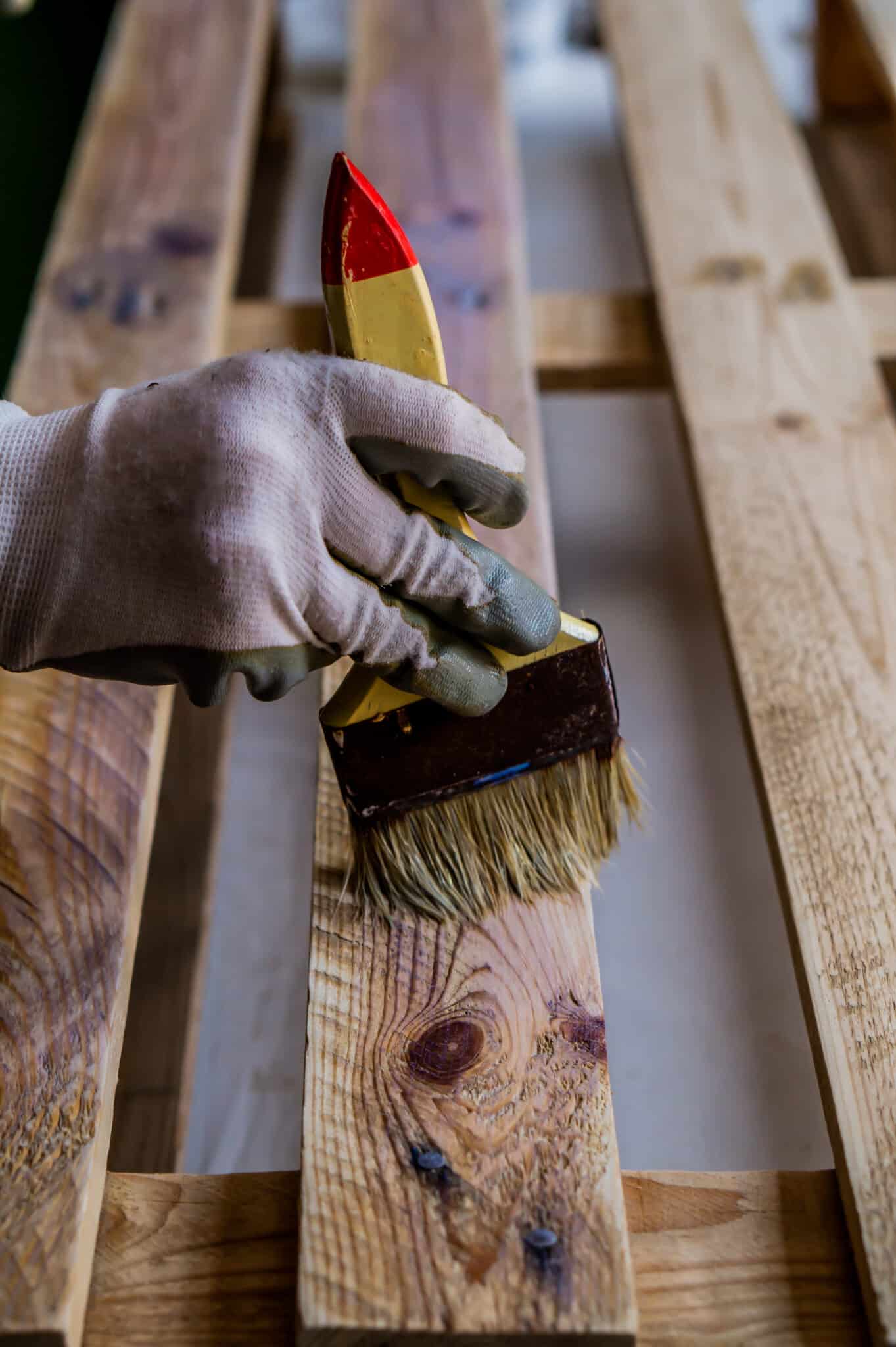 A vertical shot of a person painting a wooden pallet with a brush