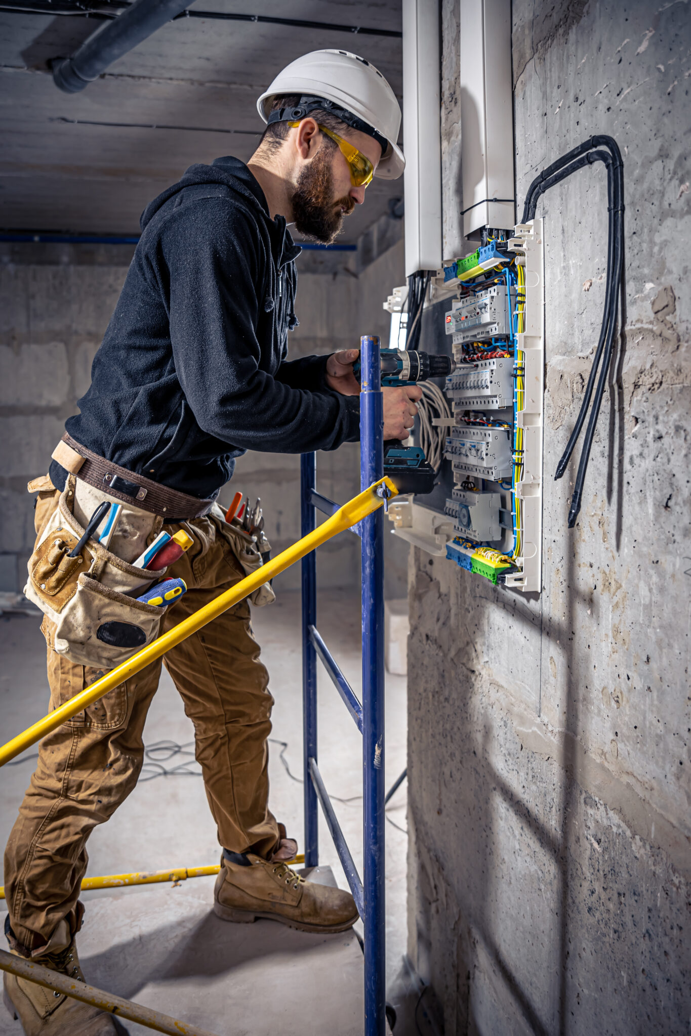 A male electrician works in a switchboard with an electrical connecting cable, connects the equipment with tools.